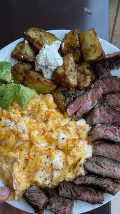 a plate with steak, potatoes, and other food on it is being held by a person