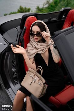 a woman sitting in the back of a car talking on a cell phone and holding a purse