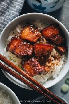 a bowl filled with rice and meat next to chopsticks on top of it