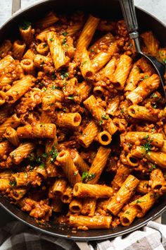 a skillet filled with pasta and sauce on top of a white cloth next to a fork