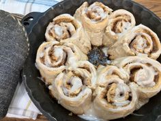 a pan filled with cinnamon rolls sitting on top of a wooden table next to a cloth