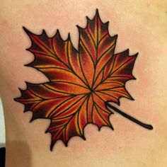 a leaf tattoo on the back of a woman's upper body, with red and yellow leaves