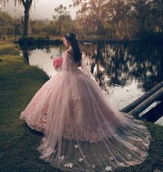 a woman in a pink dress is standing by the water with flowers on her wedding gown