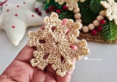 a hand holding a crocheted snowflake ornament in front of christmas decorations