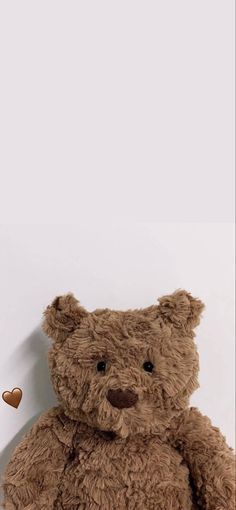 a brown teddy bear sitting on top of a white wall next to a heart shaped object