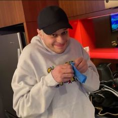 a man in a white sweatshirt and black hat holding a blue pair of scissors