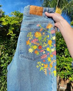 someone is holding up their jeans with embroidered flowers on them and palm trees in the background