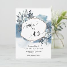 save the date card with blue watercolor flowers and greenery on white marble background