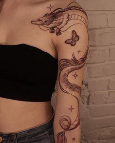 a woman with a dragon and butterfly tattoo on her arm, next to a brick wall