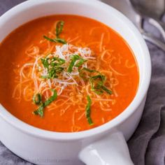 a white bowl filled with tomato soup topped with parmesan cheese and green onions