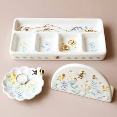 two trays with rings on them sitting next to a ring dish and bracelet holder