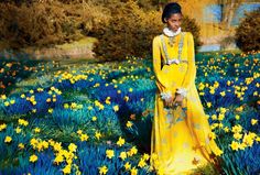 a woman in a yellow dress standing in a field of flowers