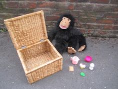 a stuffed monkey sitting next to an empty basket and toy bottles on the ground near a brick wall