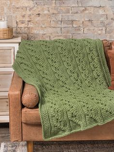 a couch with a green blanket on top of it next to a wooden table and brick wall