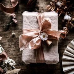 a wrapped present sitting on top of a wooden table next to other wrapping supplies and flowers