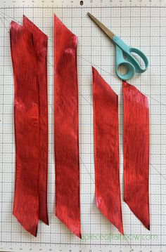 three pieces of red fabric being cut with scissors on a piece of cutting paper next to each other