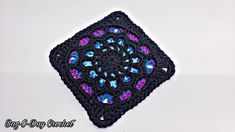 a crocheted square with blue, pink and purple flowers on it sitting on a white surface