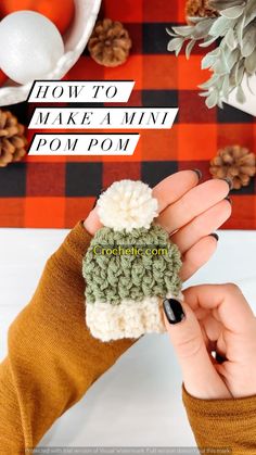 a woman's hand holding up a small crocheted hat with pom pom