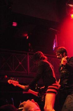 two people standing on stage with microphones in their hands and one person holding an electric guitar