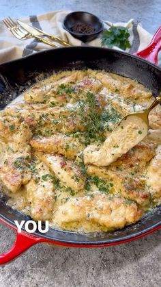 a skillet filled with chicken and sauce on top of a table next to a fork