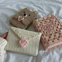 four crocheted purses on a bed with a teddy bear in the middle