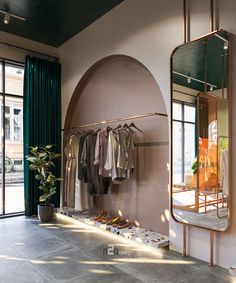 a clothing rack in front of a mirror with clothes hanging on it and a potted plant next to it