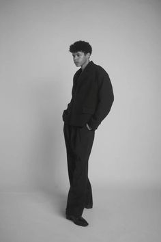 a man standing in front of a white wall wearing black pants and a black shirt