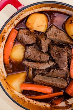 pot roast with carrots, potatoes and gravy in a red pan on a wooden table