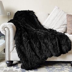 a white couch with a black furry blanket on it's back in a living room