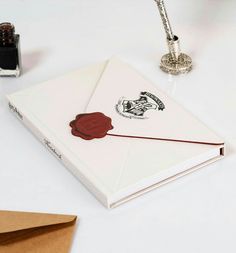 an open book with a wax stamp on it next to a pen and inkwell