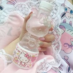 a hand holding a baby bottle with hello kitty on the lid and lace around it