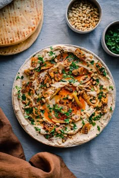 an uncooked pita bread topped with nuts and herbs next to other ingredients