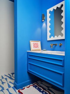 a bathroom with blue walls and white counter tops, an art work on the wall