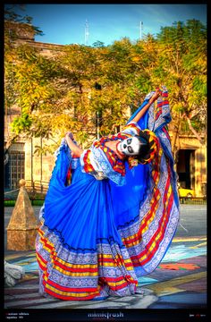 a woman in a blue and red dress is dancing on the street with her hands behind her head