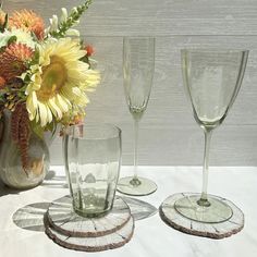 three wine glasses sitting on top of a table next to a vase filled with flowers