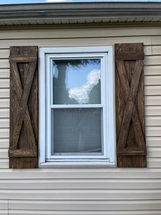 a window with wooden shutters on the side of a white house in front of a blue sky