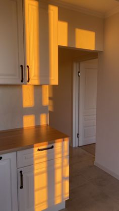 an empty kitchen with white cabinets and light coming in from the window on the far wall