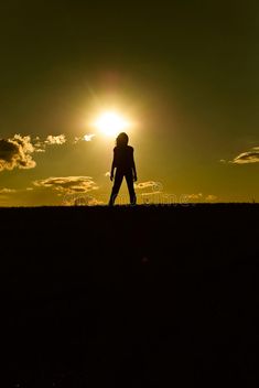 the silhouette of a person walking across a field with the sun setting in the background