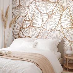 a white bed sitting next to a wall covered in gold leafy art deco stencils