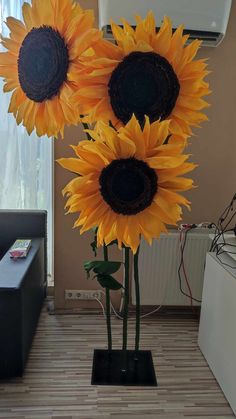 three large sunflowers in a black vase on a table next to a couch