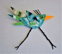 a colorful bird made out of yarn sitting on top of a table next to a white wall