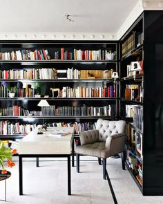 a room filled with lots of books and chairs next to a table in front of a book shelf