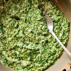 a bowl filled with spinach on top of a table next to a silver spoon