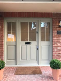 two potted plants sit outside the front door of a brick building with glass doors