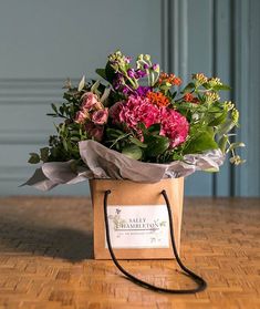 a bouquet of flowers in a brown paper bag on a wooden table with a name tag