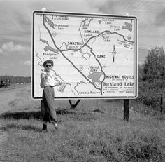 a woman standing in front of a sign with a map on it's side