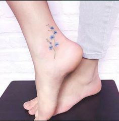 a woman's foot with a small blue flower tattoo on her left side ankle