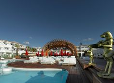 an outdoor swimming pool with lounge chairs and a statue in the foreground, surrounded by buildings