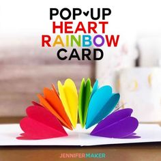 the pop - up heart rainbow card is open and has colorful feathers on top of it