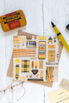 an assortment of crafting supplies on top of a white wooden table next to a pair of eyeglasses